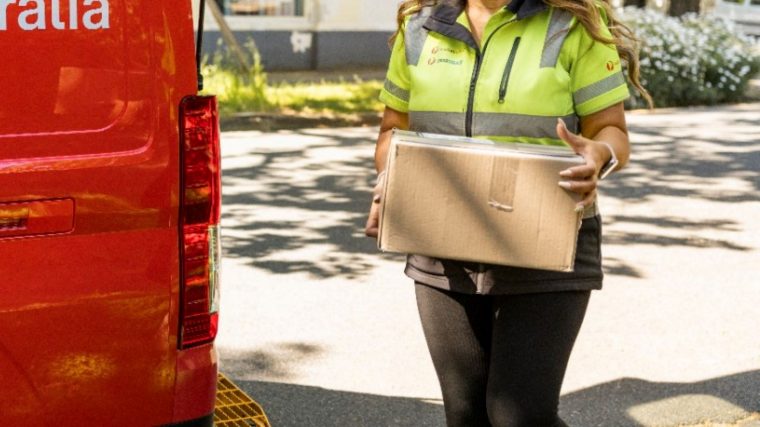 photo female postie holding package next to australia post van.jpg.auspostimage.760 0.169.medium